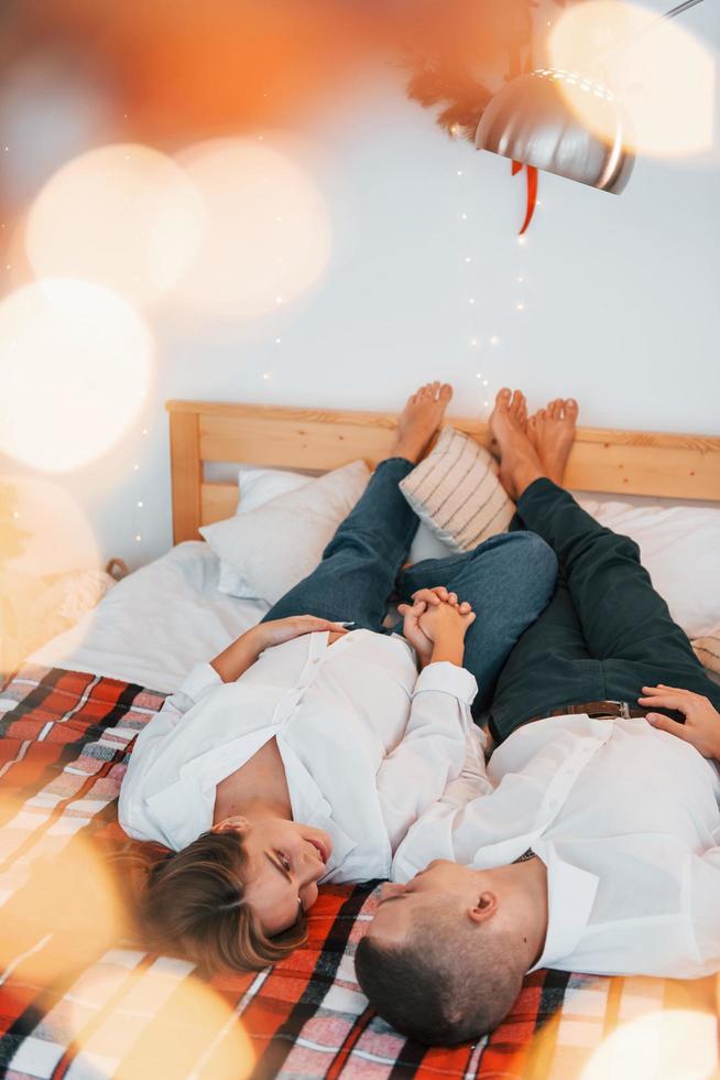 houdende naar beneden Aan de bed. lief paar vieren vakantie samen binnenshuis foto