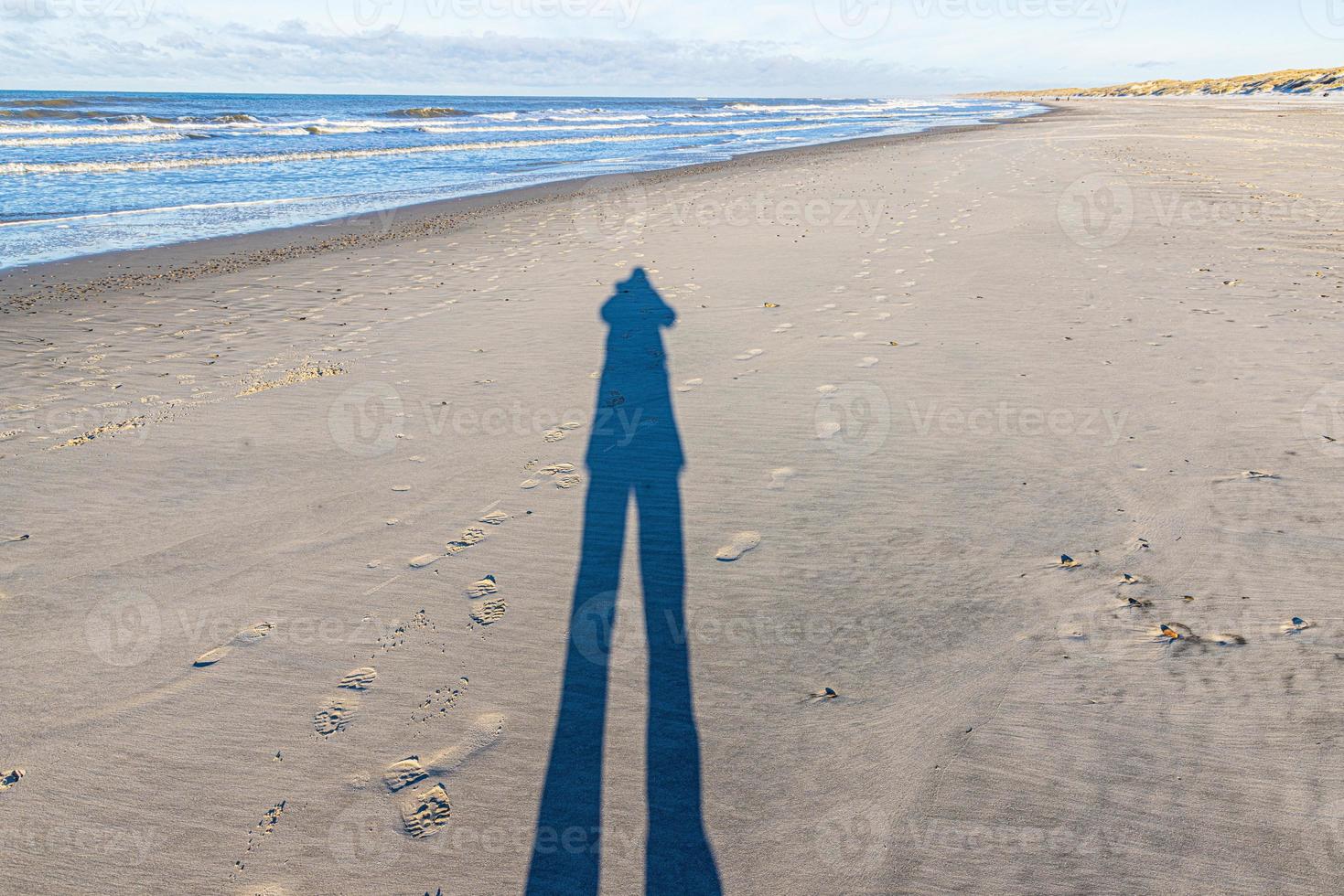 beeld van een lang schaduw van een persoon Aan een breed zanderig strand foto