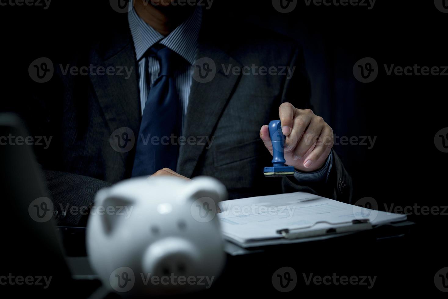 zakenman is stempelen een rubber postzegel Aan een financieel en bank goedkeuring document of papier contract overeenkomst Aan bureau. foto