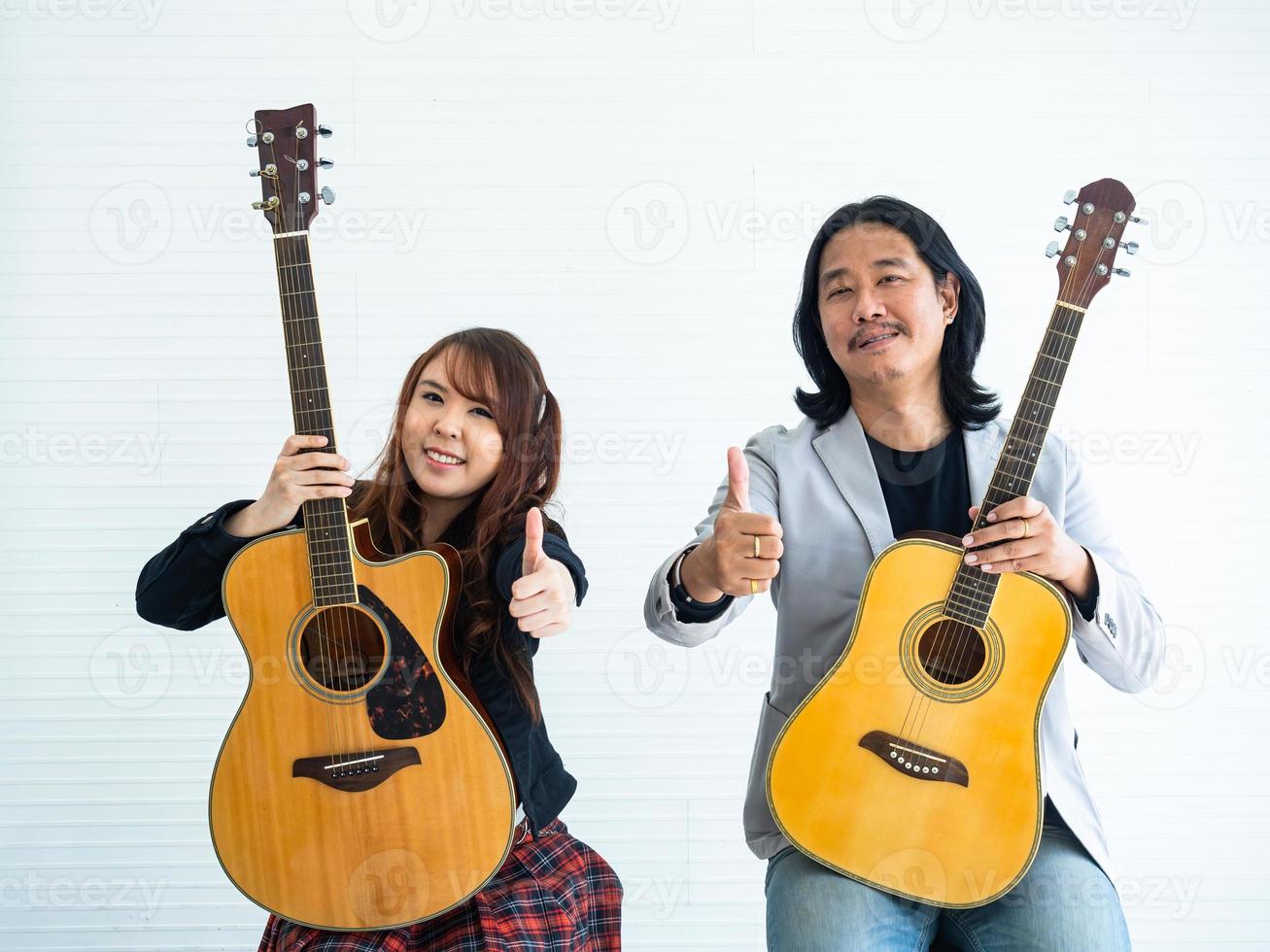 portret van Aziatisch duo artiesten met een akoestisch gitaar zittend Aan een wit achtergrond en tonen de gebaar van bonzen omhoog voor muziek, artiest, musicus concept foto