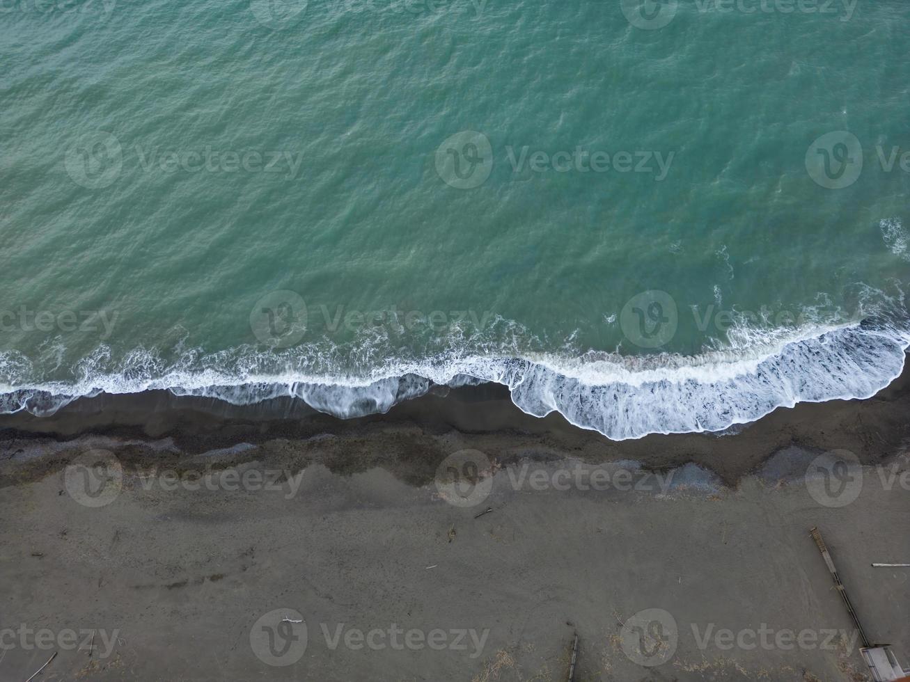antenne visie van donker strand met klein golven spatten foto