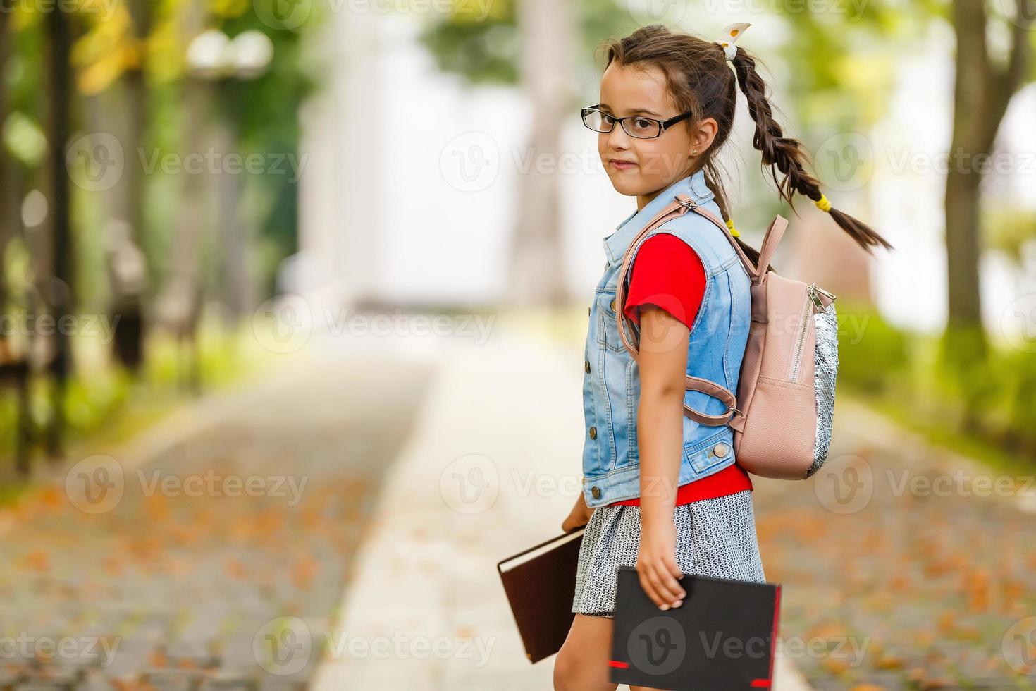 kind gaan terug naar school. begin van nieuw school- jaar na zomer vakantie. weinig meisje met rugzak en boeken Aan eerste school- dag. begin van klas. onderwijs voor kleuterschool en peuter- kinderen. foto