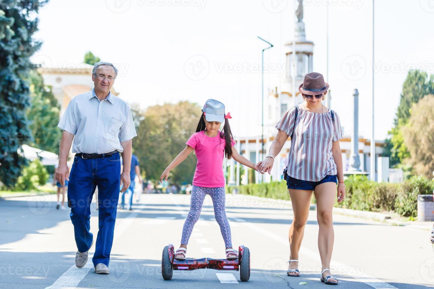 weinig glimlachen meisje aan het leren naar rijden een hoverboard met haar ouders buitenshuis foto