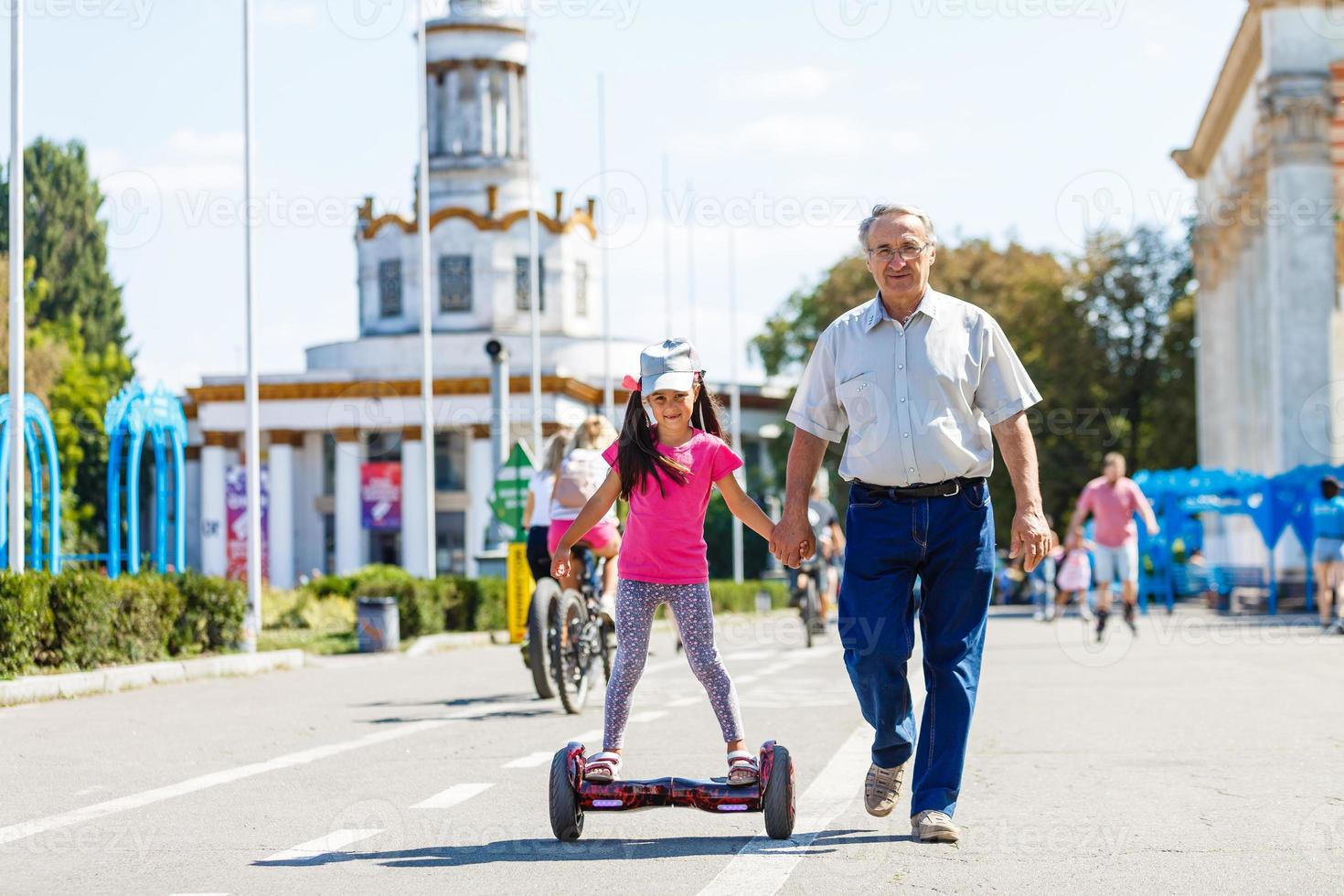 weinig glimlachen meisje aan het leren naar rijden een hoverboard met haar ouders buitenshuis foto