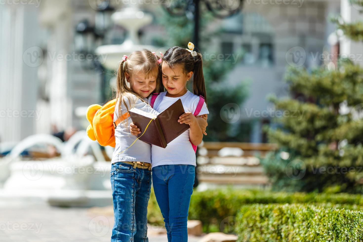 twee school- meisjes vervelend rugzak buiten de primair school. schoolmeisje, elementair school- leerling gaan van school, diploma uitreiking, zomer vakantie. foto