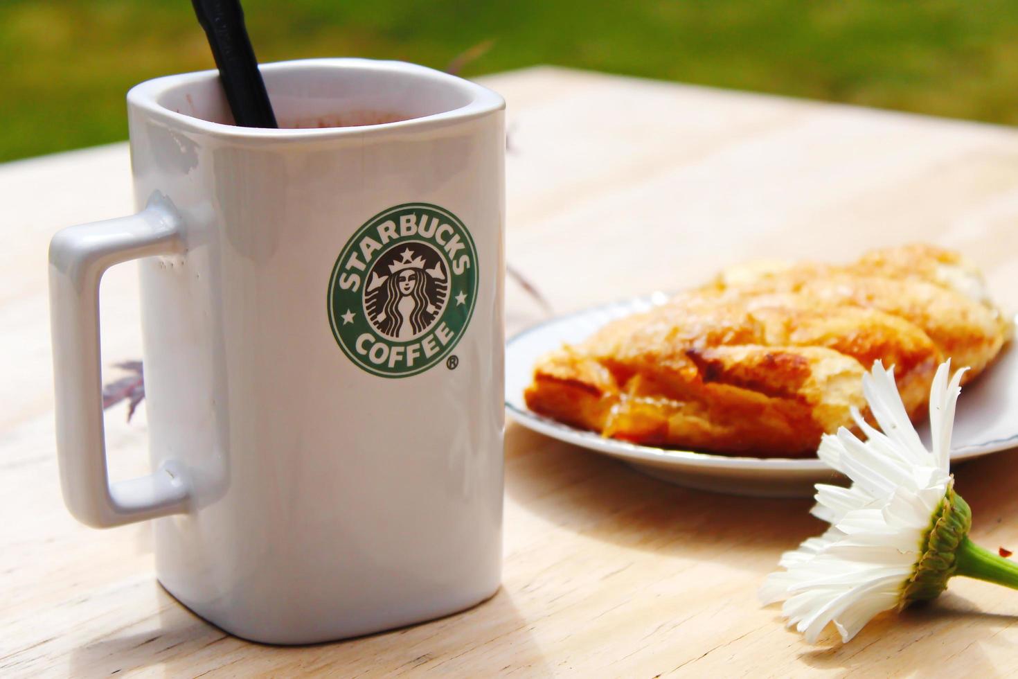 Washington, Verenigde Staten van Amerika - augustus 01 2022 koffie mok met Starbucks logo Aan voorkant, wit bakkerij Aan bord. plaats het Aan een houten tafel in de tuin waar de ochtend- zon schijnt. foto