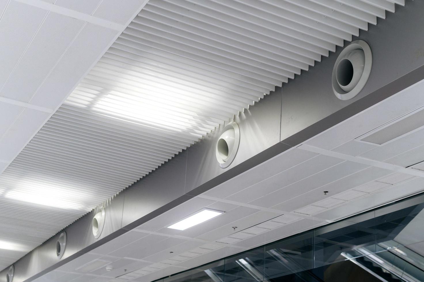 plafond gemonteerd cassette type lucht conditioner en modern lamp licht Aan wit plafond. kanaal lucht conditioner voor huis of kantoor foto