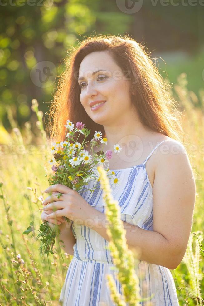 detailopname portret van mooi jong vrouw snuiven boeket van mooi wilde bloemen Aan zonnig zomer dag. concept van vreugde van communiceren met natuur foto