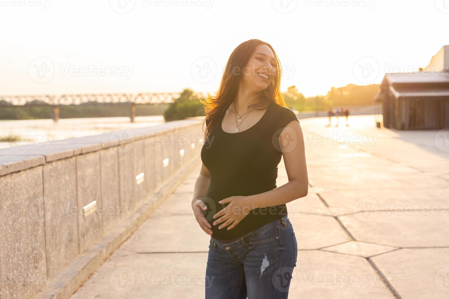 portret van spaans zwanger vrouw wandelen Aan dijk Bij zonsondergang. zwangerschap en moederschap concept. foto