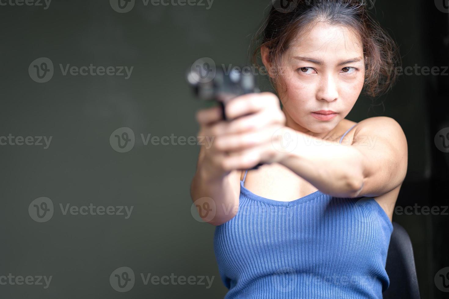 jong vrouw Holding handgeweer het richten gevaarlijk misdrijf persoon. mooi Aziatisch vrouw spion middel richten pistool vuurwapen naar verdedigen gangster, portret. vrouw het schieten een geweer wapen zelf bescherming concept foto