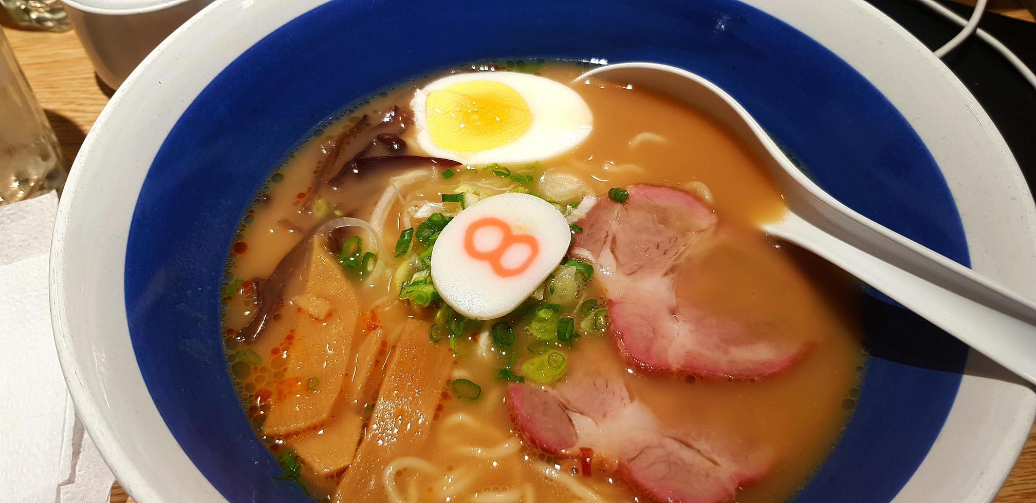 dichtbij omhoog heet hachiban ramen noodle met geroosterd varkensvlees gesneden en smakelijk soep in blauw kom Aan houten tafel Bij Japans restaurant. gezond leven stijl aan het eten en Aziatisch voedsel concept. Aziatisch voedsel met lepel. foto