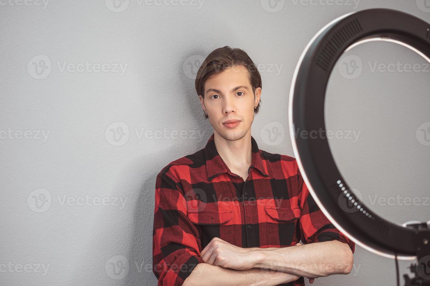 jong Mens haar- stilist in rood plaid overhemd met ring lamp Aan de grijs muur achtergrond foto