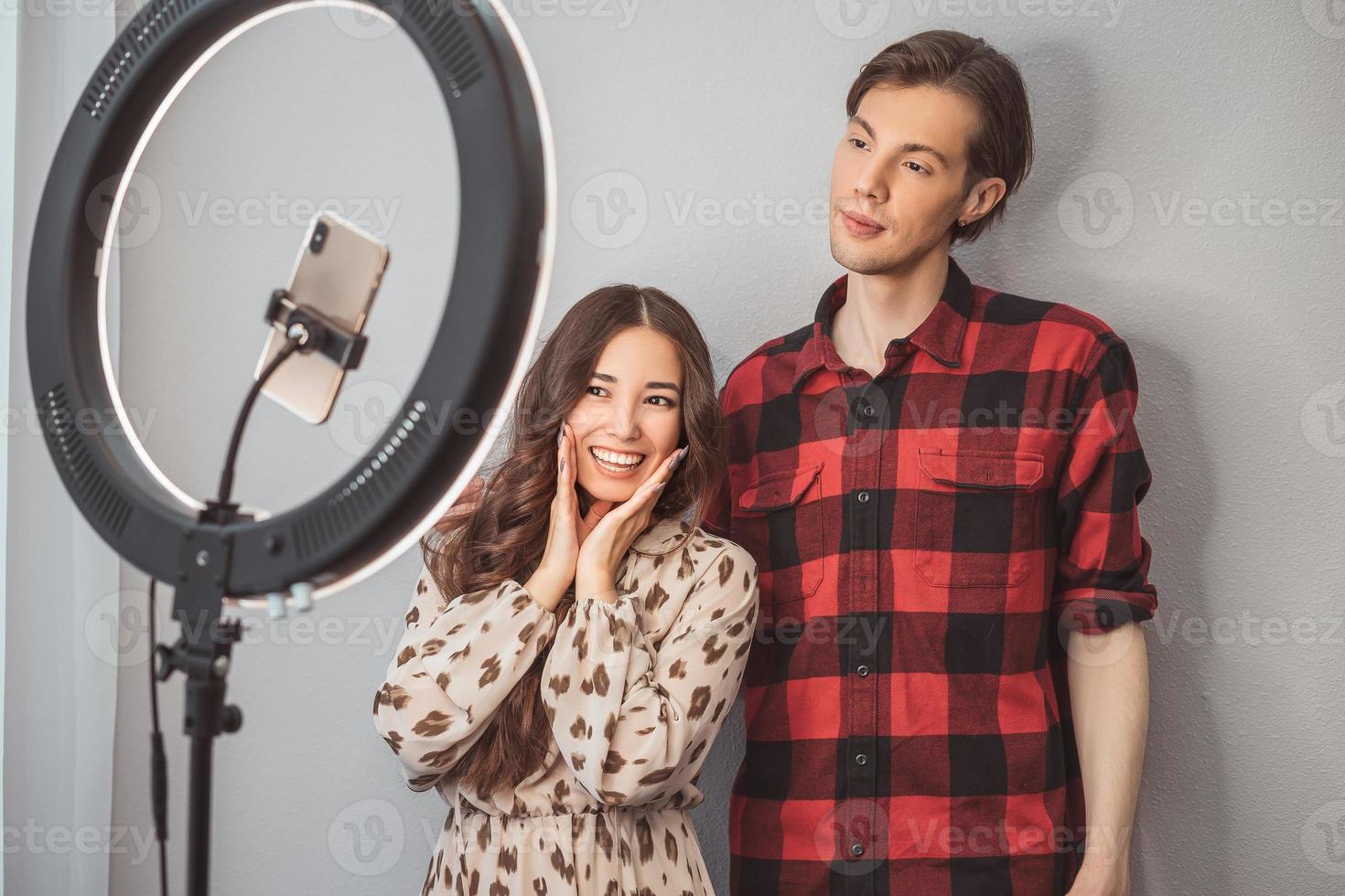 jong paar van schoonheid bloggers, haar- stilist, kapper en model- met haar- stijl schieten Aan mobiel telefoon met ring lamp Aan de grijs muur achtergrond foto