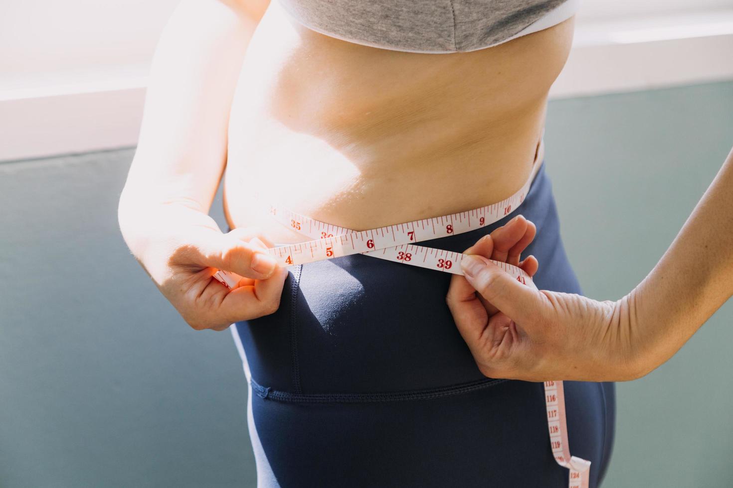 mooie dikke vrouw met meetlint ze gebruikt haar hand om het overtollige vet dat op een witte achtergrond is geïsoleerd uit te knijpen. ze wil afvallen, het concept van chirurgie en vet afbreken onder de foto