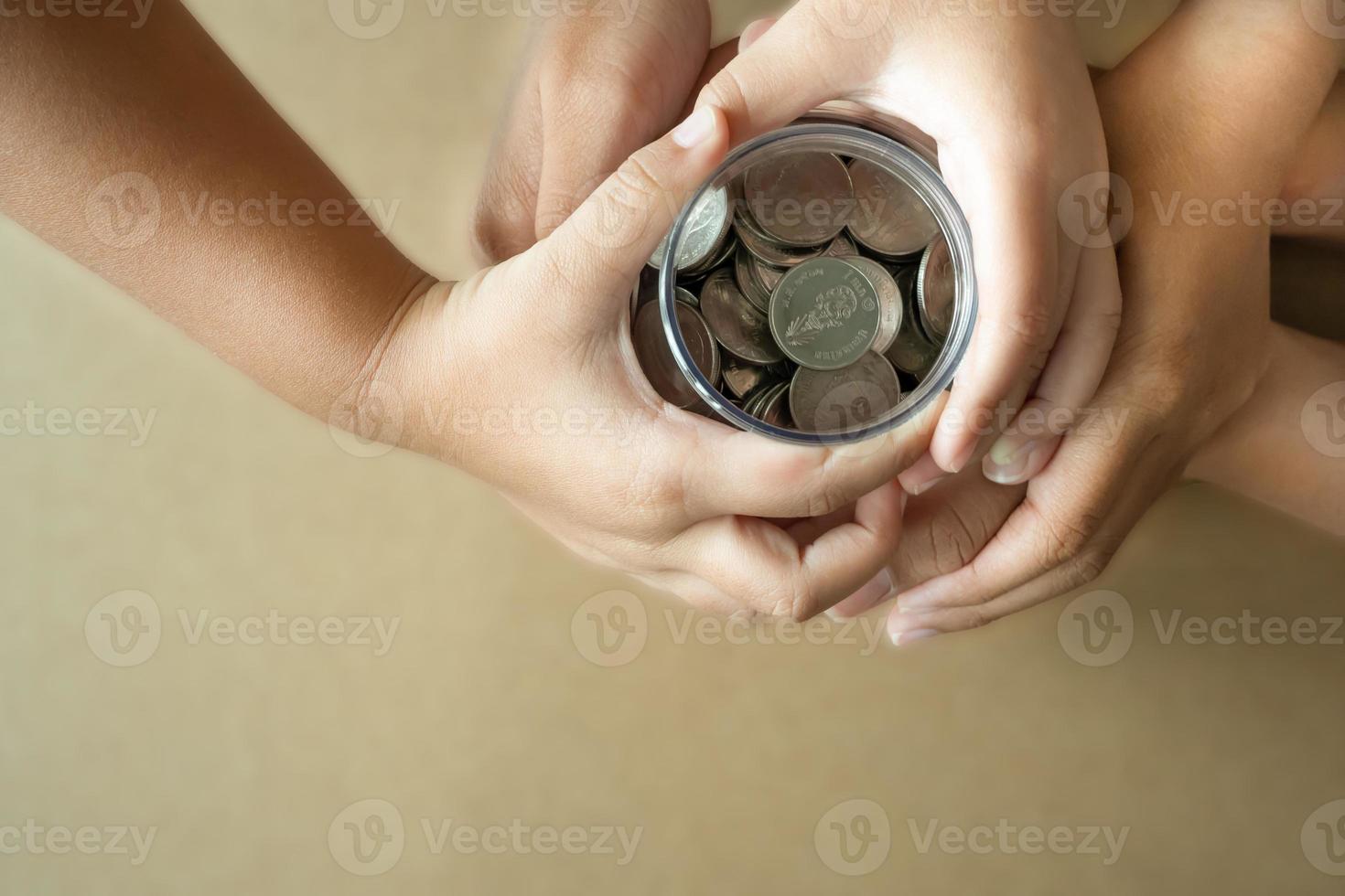 kind handen Holding munten in een pot samen net zo besparing concept voor familie of onderwijs. foto