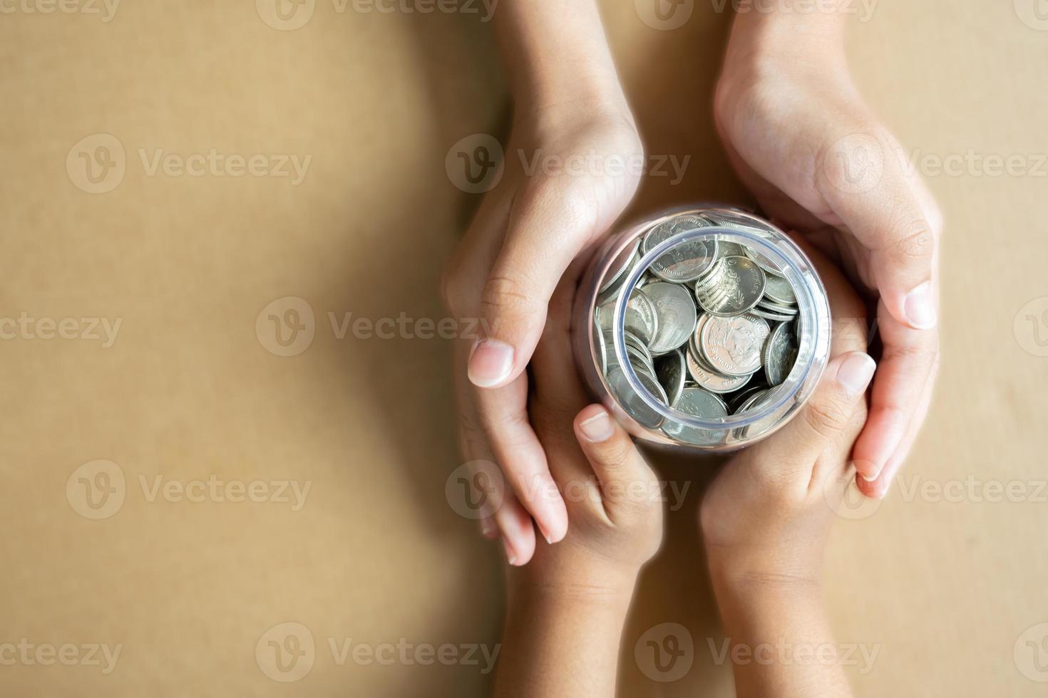 kind handen Holding munten in een pot samen net zo besparing concept voor familie of onderwijs. foto