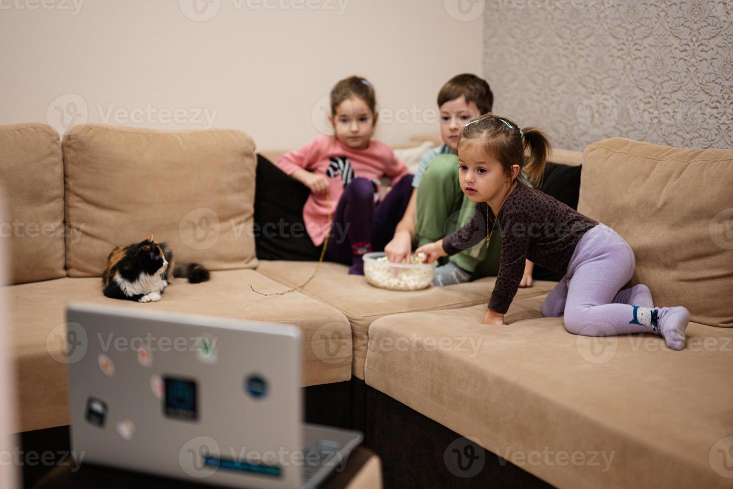 drie kinderen met katje zittend Aan de leven kamer aan het kijken film of tekenfilm van laptop. foto