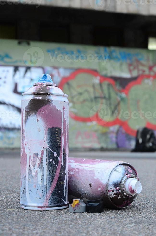 meerdere gebruikt verstuiven blikjes met roze en wit verf en petten voor sproeien verf onder druk is leugens Aan de asfalt in de buurt de geschilderd muur in gekleurde graffiti tekeningen foto