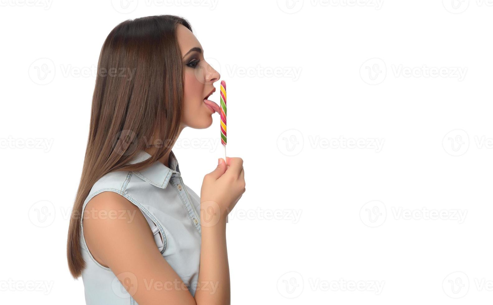 vrouw likken zoet snoep. vrouw model- aan het eten heerlijk banketbakkerij lolly met verrast uitdrukking. studio schot geïsoleerd wit achtergrond foto
