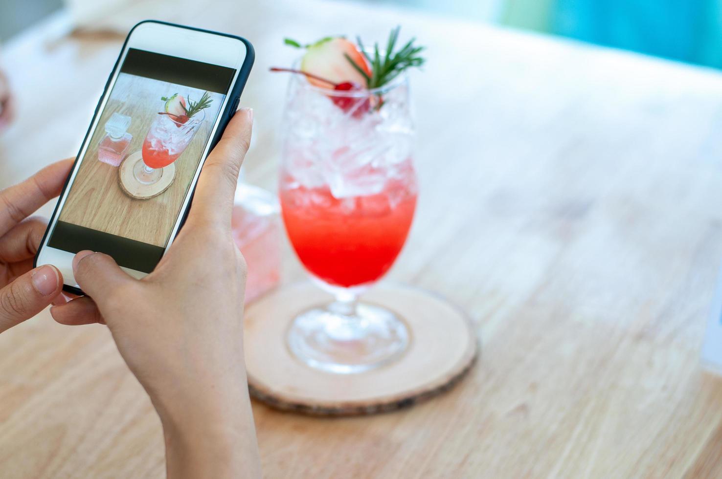 een vrouw toepassingen een smartphone naar nemen een afbeelding van een aardbei Frisdrank drinken in een koffie winkel naar uploaden naar sociaal media. kom tot rust in cafe foto