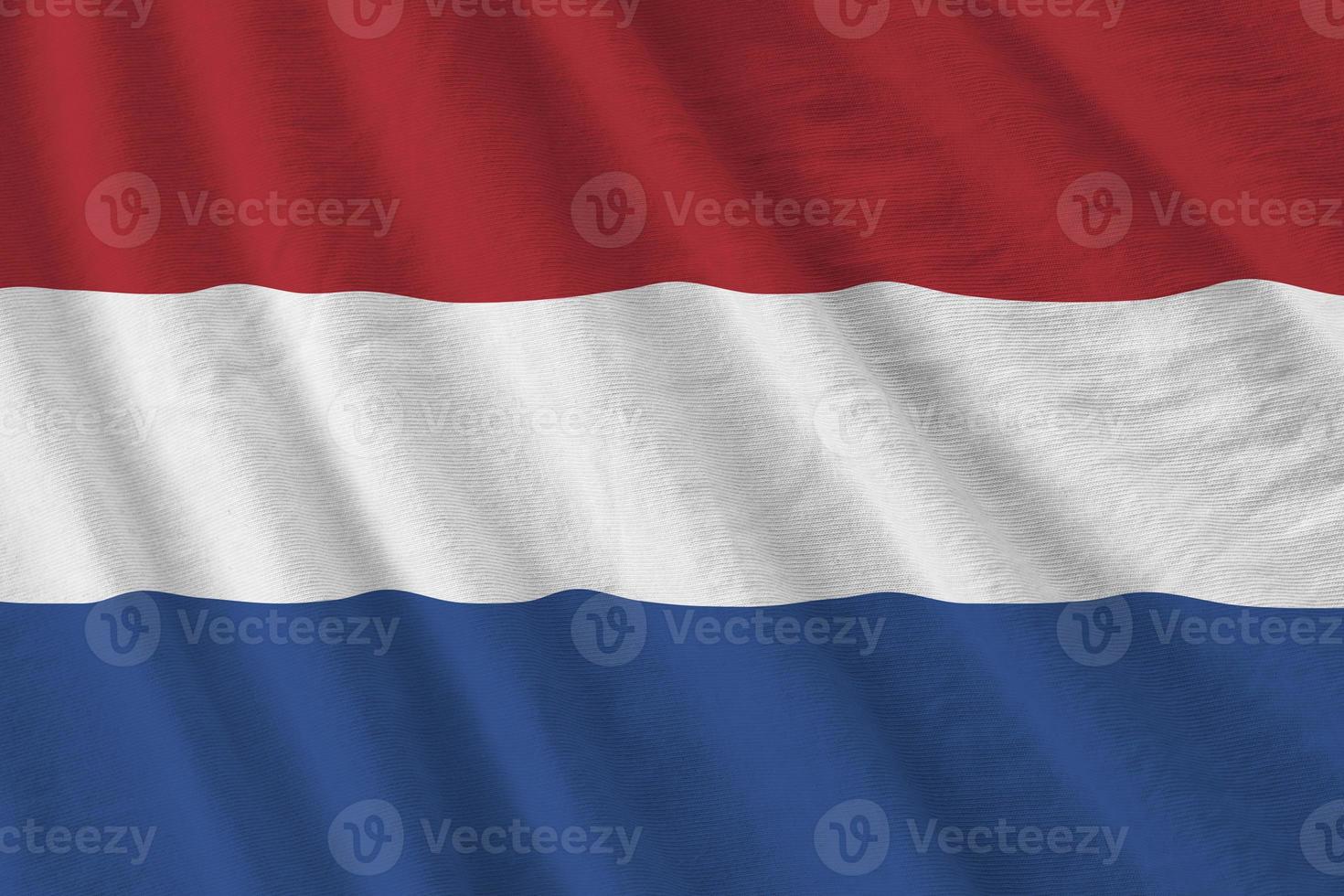 Nederland vlag met groot vouwen golvend dichtbij omhoog onder de studio licht binnenshuis. de officieel symbolen en kleuren in banier foto