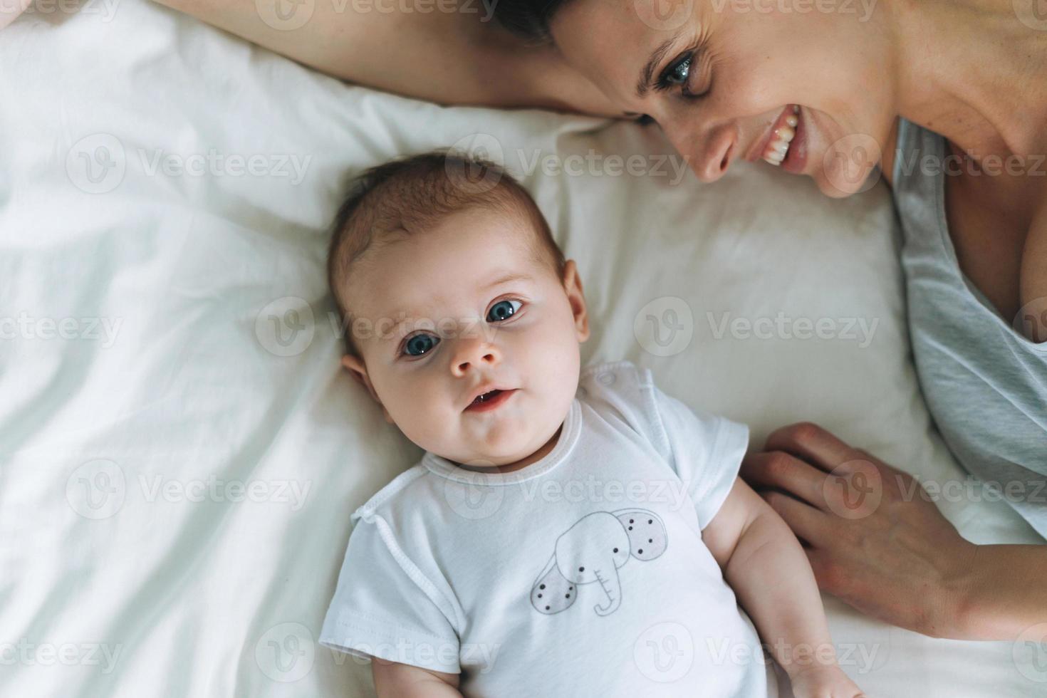 jong moeder hebben pret met schattig baby meisje Aan bed, natuurlijk tonen, liefde emotie foto