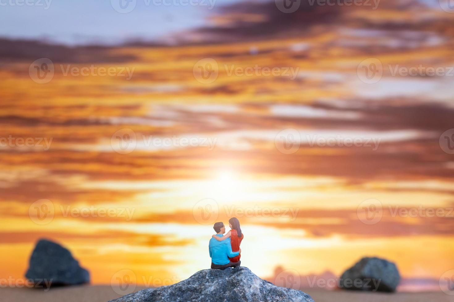 miniatuur mensen , paar zittend Aan een zee strand met zonsondergang achtergrond foto