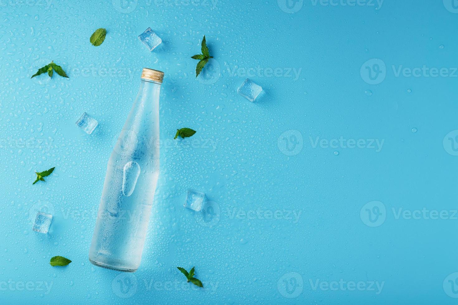 een fles van ijs water, ijs kubussen, druppels en munt bladeren Aan een blauw achtergrond. foto