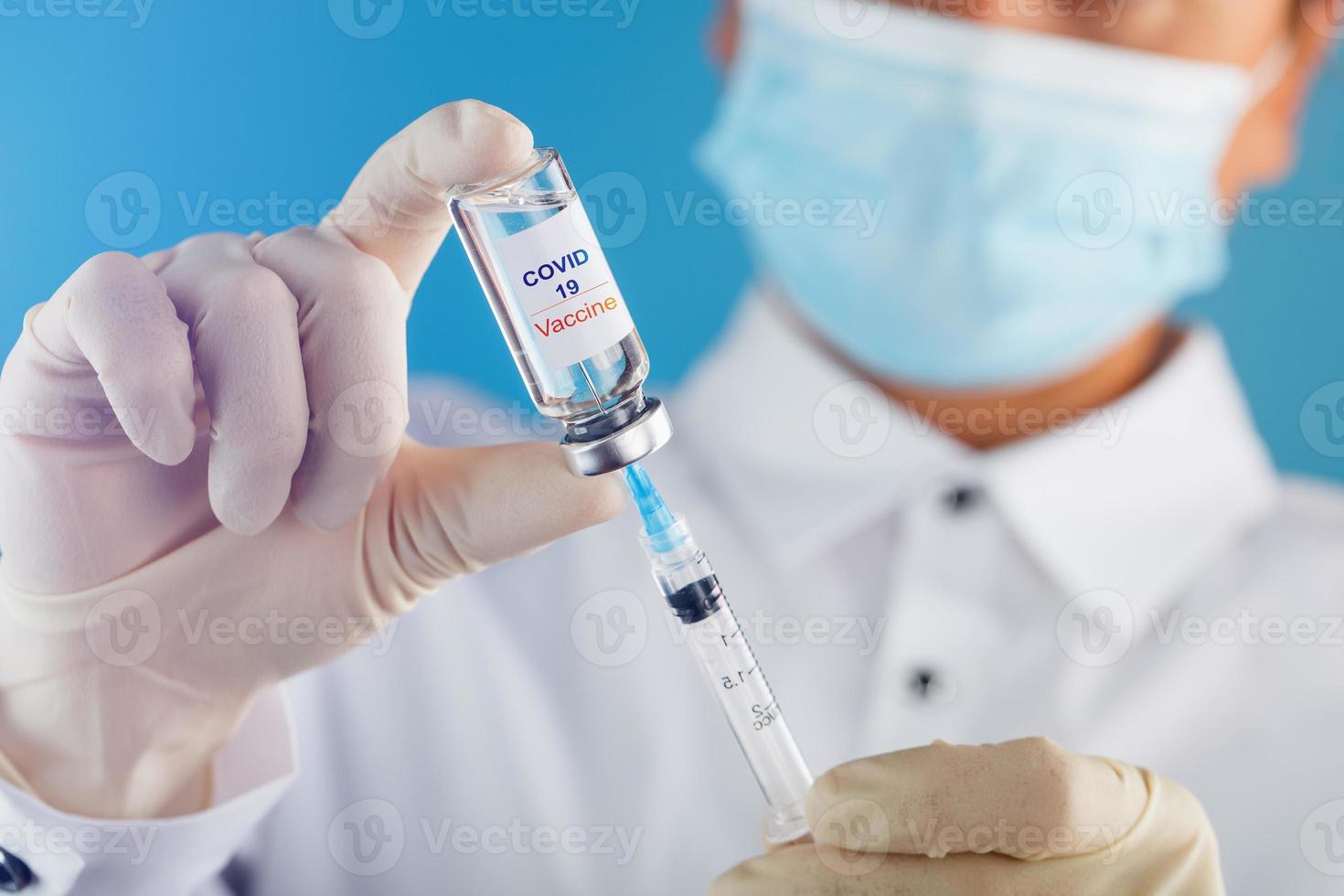 een dokter in rubber handschoenen duurt geneeskunde met een vaccin van een ampul met een injectiespuit met de tekst covid -19 Aan de ampul sticker. foto