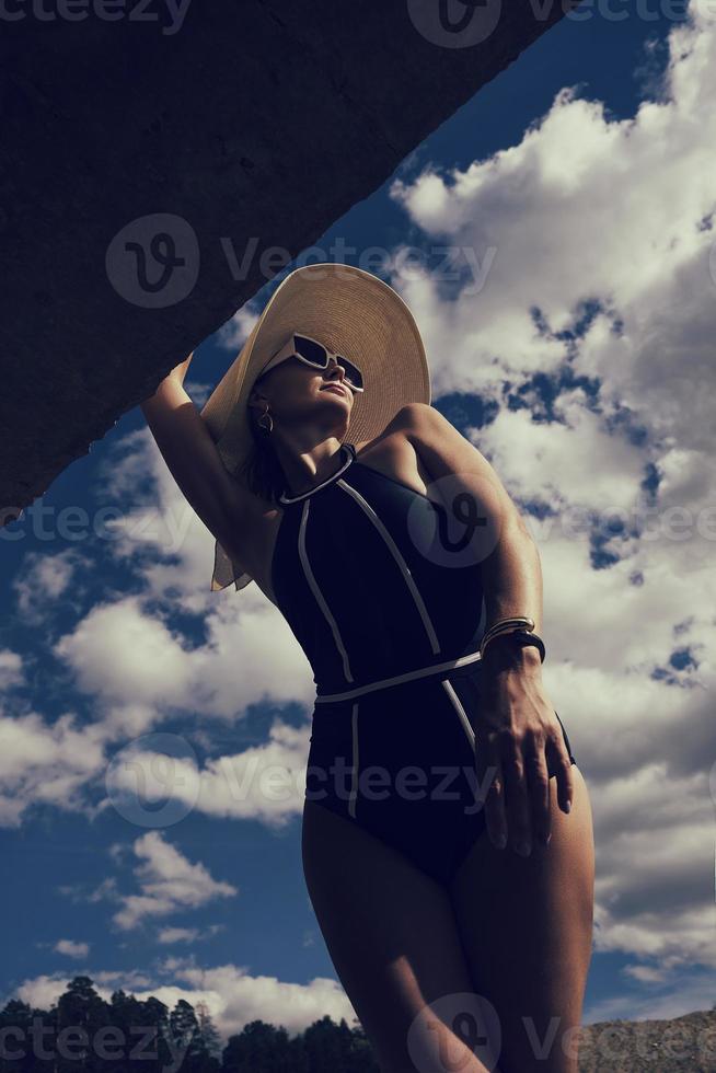 portret van een vrouw in een zwempak, hoed en zonnebril in zomer Aan de oever van de rivier tegen de lucht foto