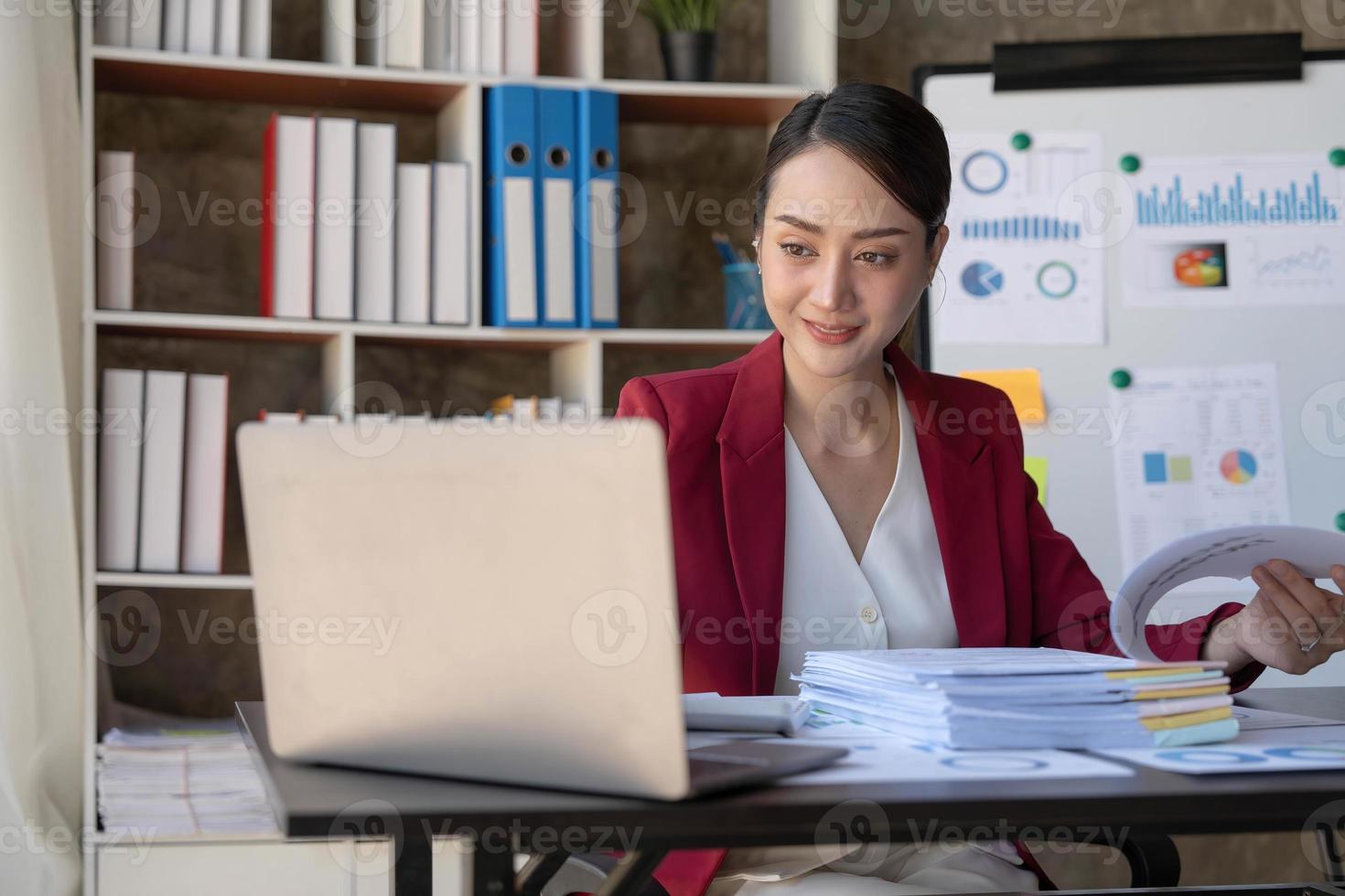 Aziatische zakenvrouw die een laptopcomputer gebruikt en op kantoor werkt met een rekenmachinedocument op het bureau, planning analyseert van het financiële rapport, businessplaninvestering, financiële analyseconcept. foto