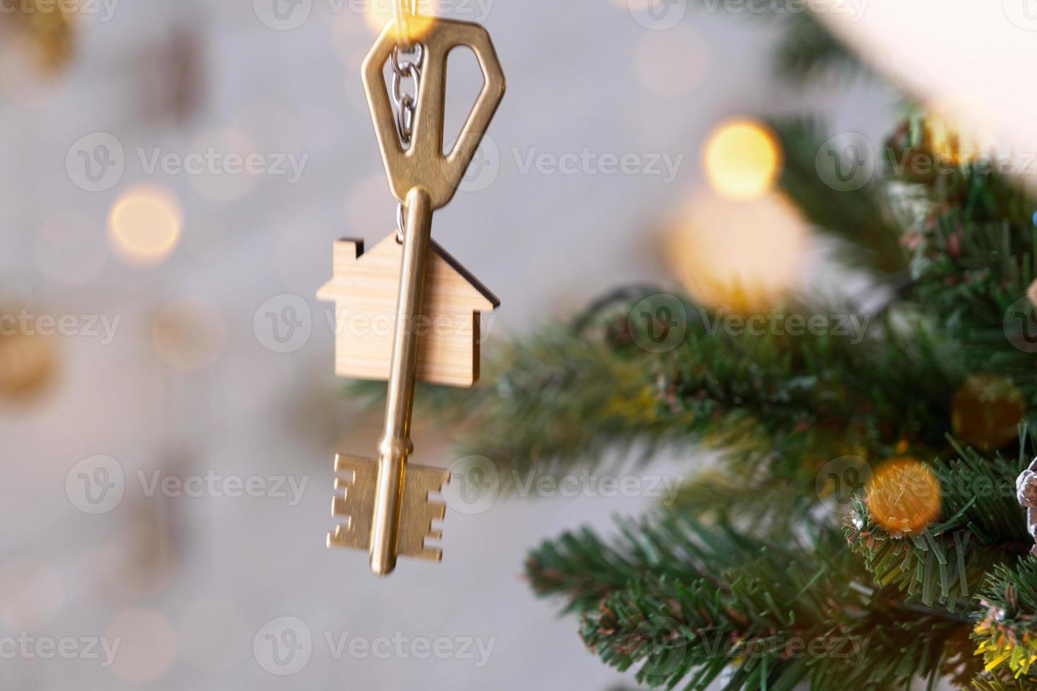 sleutel van het huis met een sleutelhanger hangt aan de kerstboom. een cadeau voor het nieuwe jaar, kerstmis. bouwen, ontwerp, project, verhuizen naar nieuw huis, hypotheek, huur en aankoop onroerend goed. kopieer ruimte foto