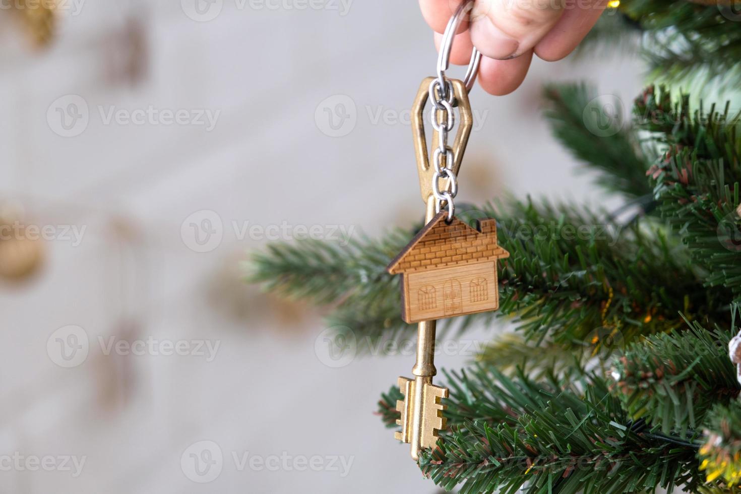 sleutel van het huis met een sleutelhanger hangt aan de kerstboom. een cadeau voor het nieuwe jaar, kerstmis. bouwen, ontwerp, project, verhuizen naar nieuw huis, hypotheek, huur en aankoop onroerend goed. kopieer ruimte foto