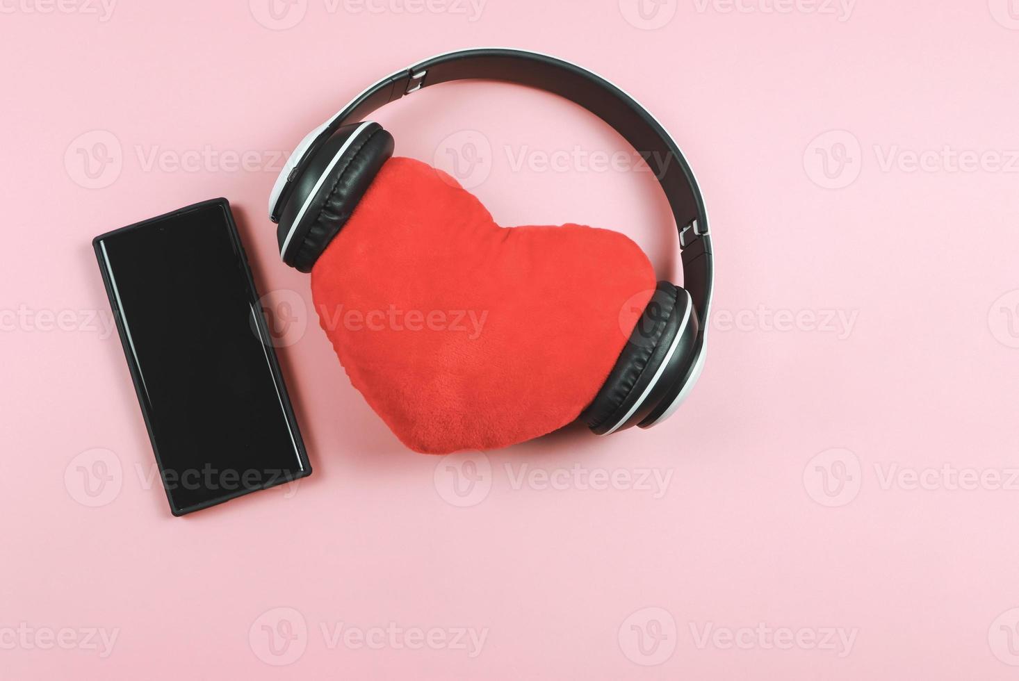 vlak leggen van rood hart hoofdkussen bedekken met hoofdtelefoons en blanco zwart scherm mobiel telefoon Aan roze achtergrond. liefde liedjes of podcast concept. foto