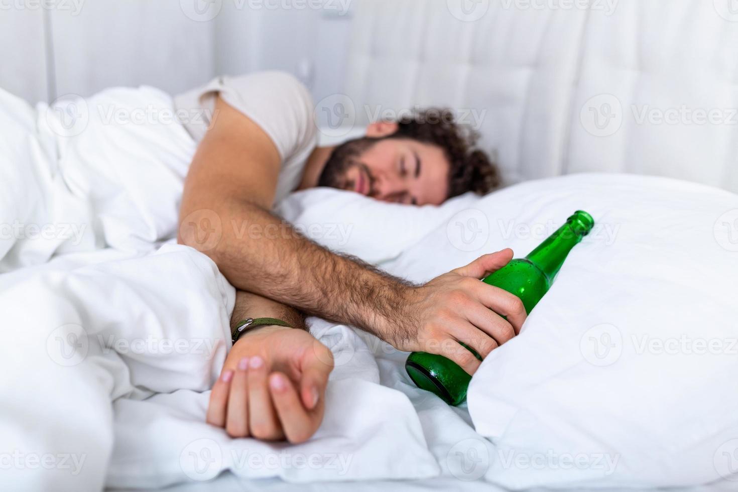 dronken Mens in de bed en verdrietig plaats en een alcohol fles in zijn hand. jong Mens aan het liegen in bed dodelijk dronken Holding bijna leeg fles van drank. foto