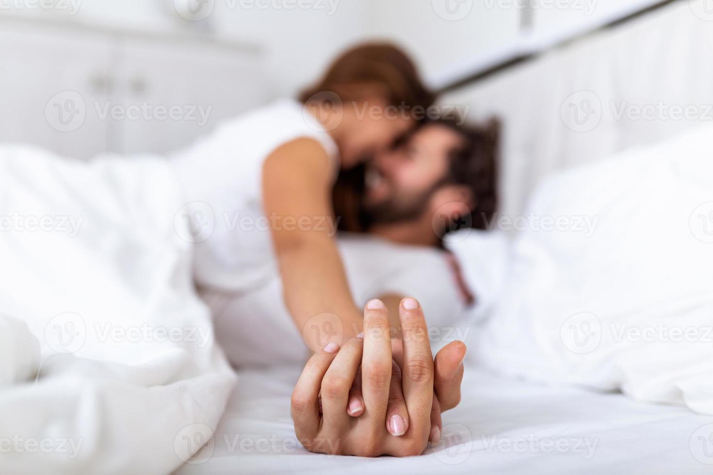 romantisch paar in bed genieten van sensueel voorspel. focus Aan handen Mens en vrouw. gelukkig sensueel jong paar aan het liegen in bed samen. mooi liefhebbend paar zoenen in bed. foto