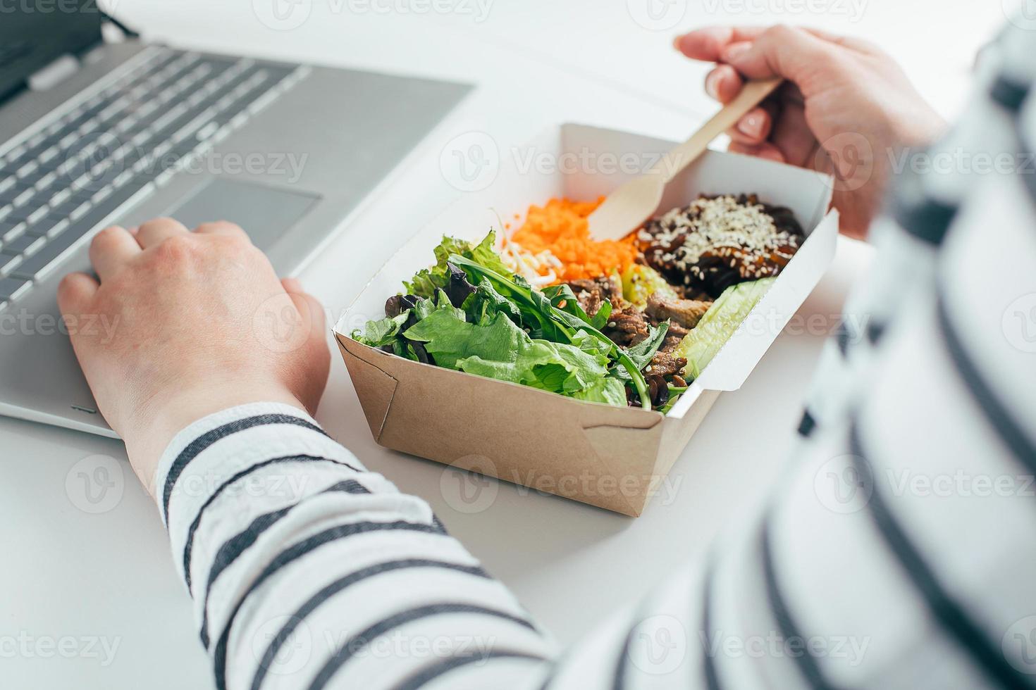 vrouw hebben lunch in gerecycled kom gebruik makend van laptop. voedsel levering, quarantaine, nemen uit voedsel concept foto