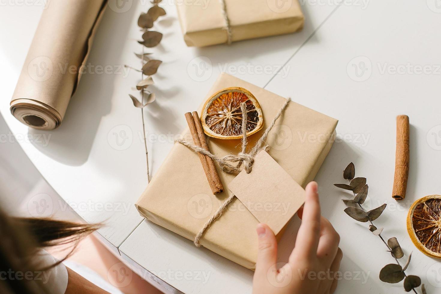 vrouw handen inpakken geschenk decor met droog oranje, kaneel stokken, eucalyptus. nul verspilling Kerstmis foto