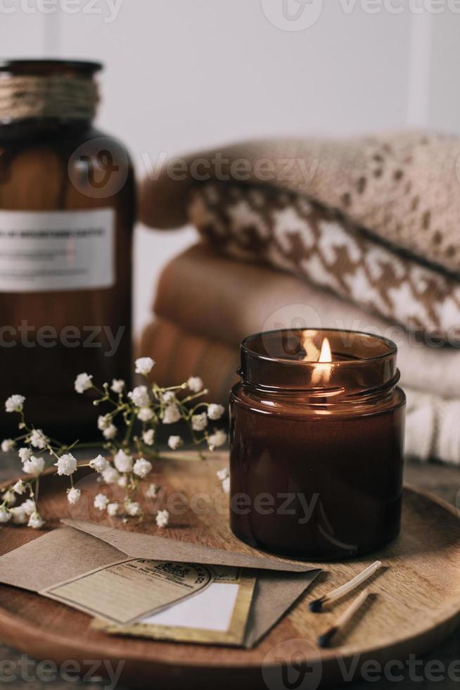 brandend kaars in klein amber glas pot met houten lont, stack gebreid seizoen truien. knus levensstijl, hygge concept foto