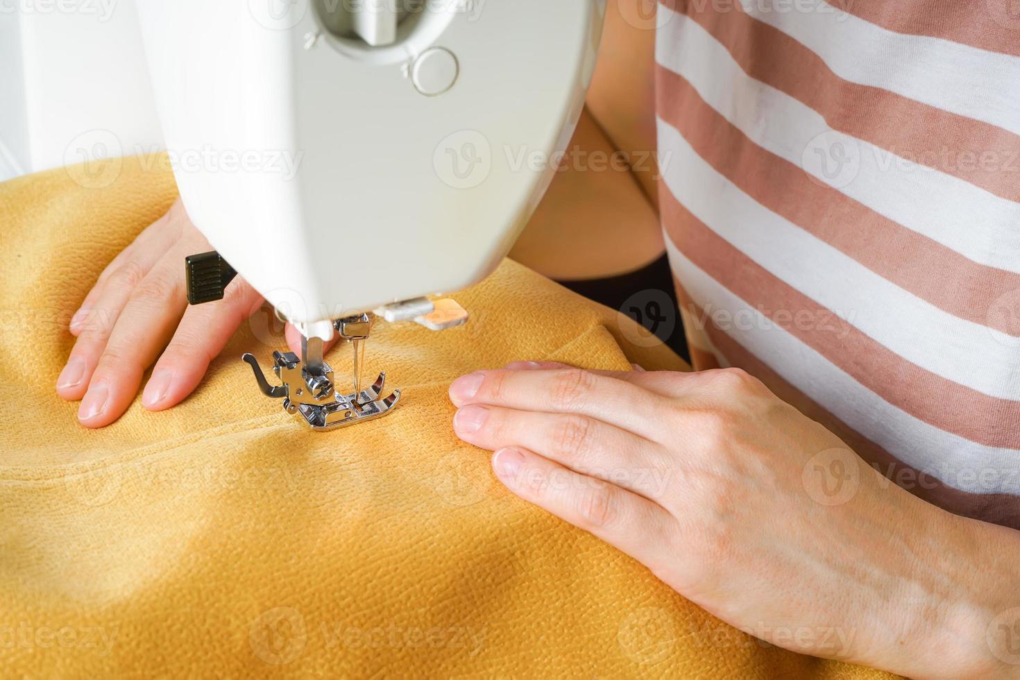 vrouw handen stiksels geel kleding stof Aan modern naaien machine. dichtbij omhoog visie van naaien werkwijze. foto