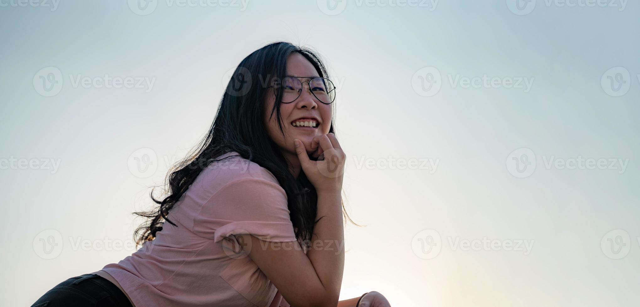 Aziatisch bril schattig vrouw houdingen voor foto het schieten Aan de op het dak verdieping naast cement terras barracade Bij schemering tijd in silhouet hoek.