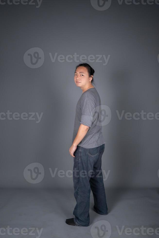 Aziatisch lang haar- vriendelijk en positief Mens is posten en staand in voorkant van grijs achtergrond met studio licht. foto