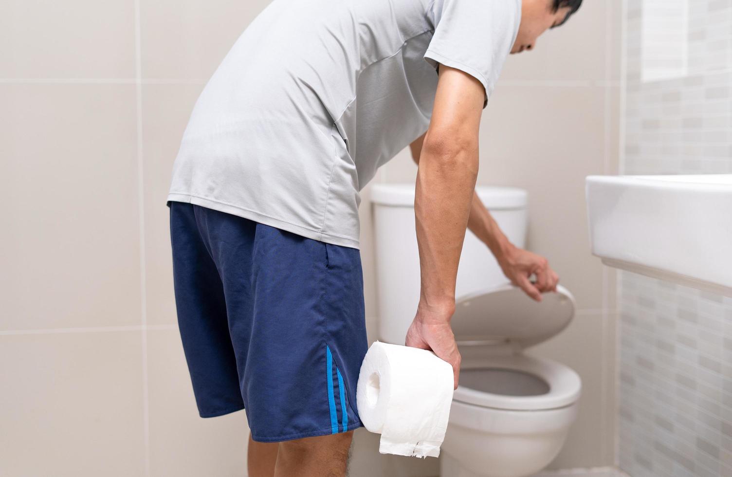 Mens staand in badkamer Holding weefsels met erge, ernstige maag pijn. maag krampen, buik pijn, diarree, dikke darm of buik kanker foto