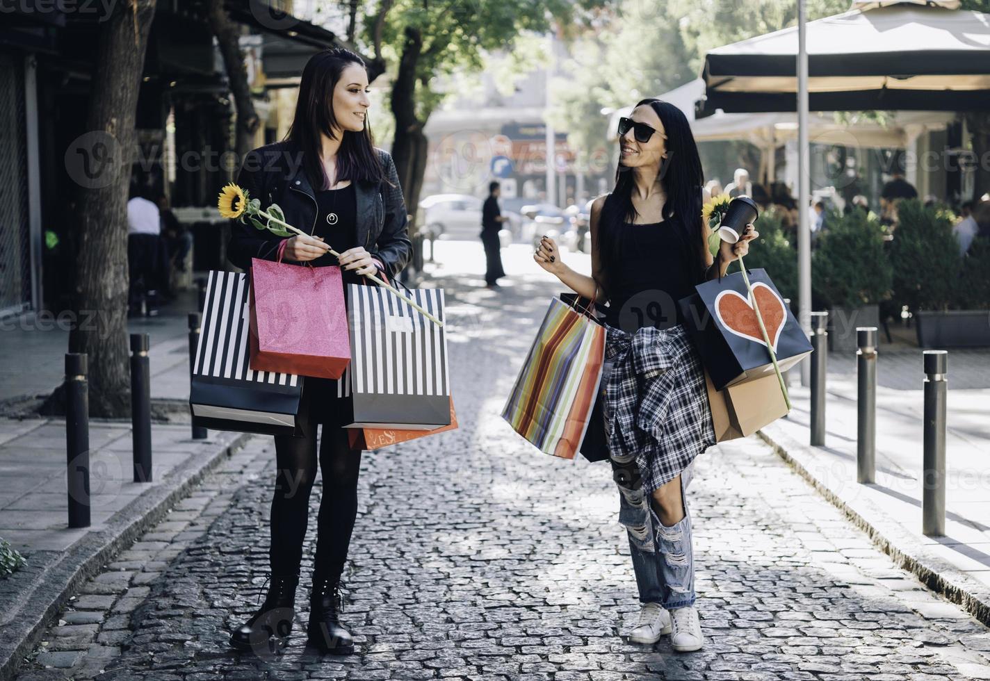 twee gelukkig vriendinnetjes op zoek Aan de etalage terwijl staand met boodschappen doen Tassen in de buurt de winkelcentrum foto