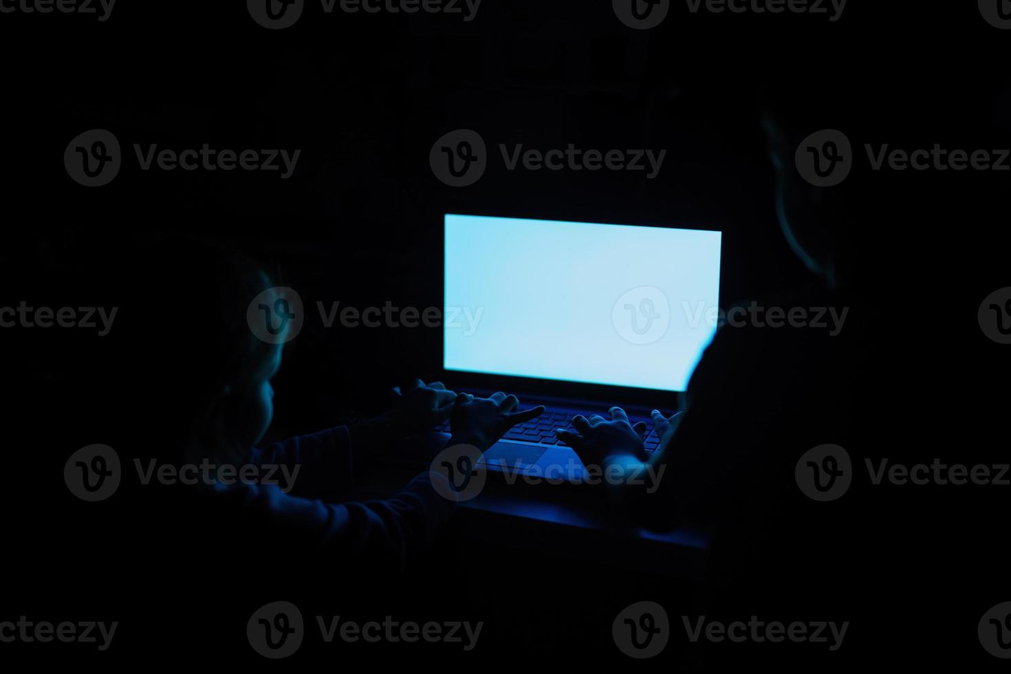 kinderen kraan Aan laptop terwijl kijk maar Aan gekleurde scherm in licht uit kamer. foto