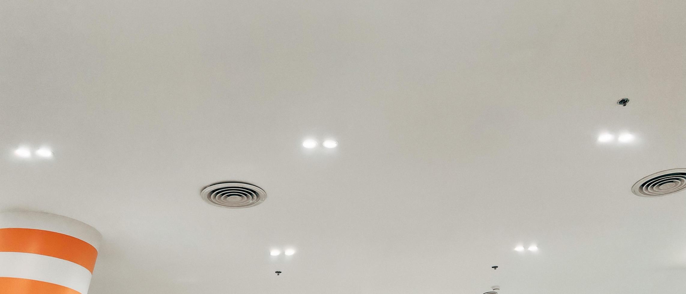 plafond gemonteerd cassette type lucht conditioner en modern lamp licht Aan wit plafond. kanaal lucht conditioner voor huis, hal of kantoor. foto