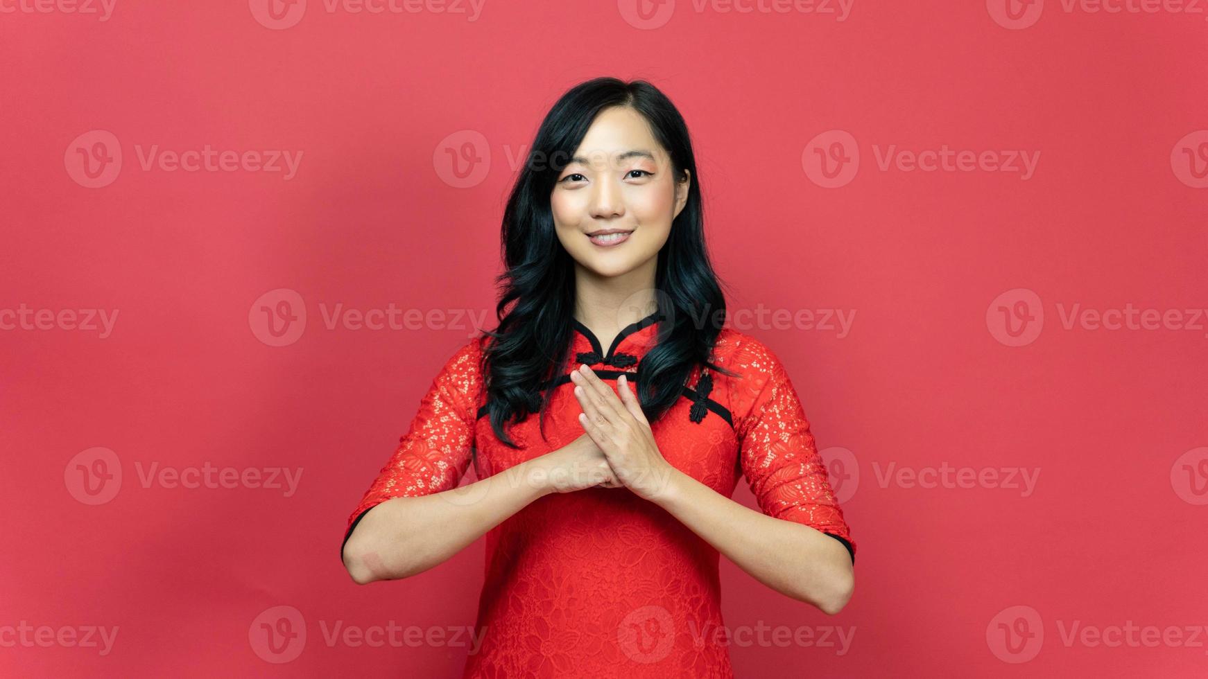 Aziatisch vrouw vervelend traditioneel cheongsam qipao jurk met gebaar van felicitatie geïsoleerd Aan rood achtergrond. gelukkig Chinese nieuw jaar. emotie glimlach foto