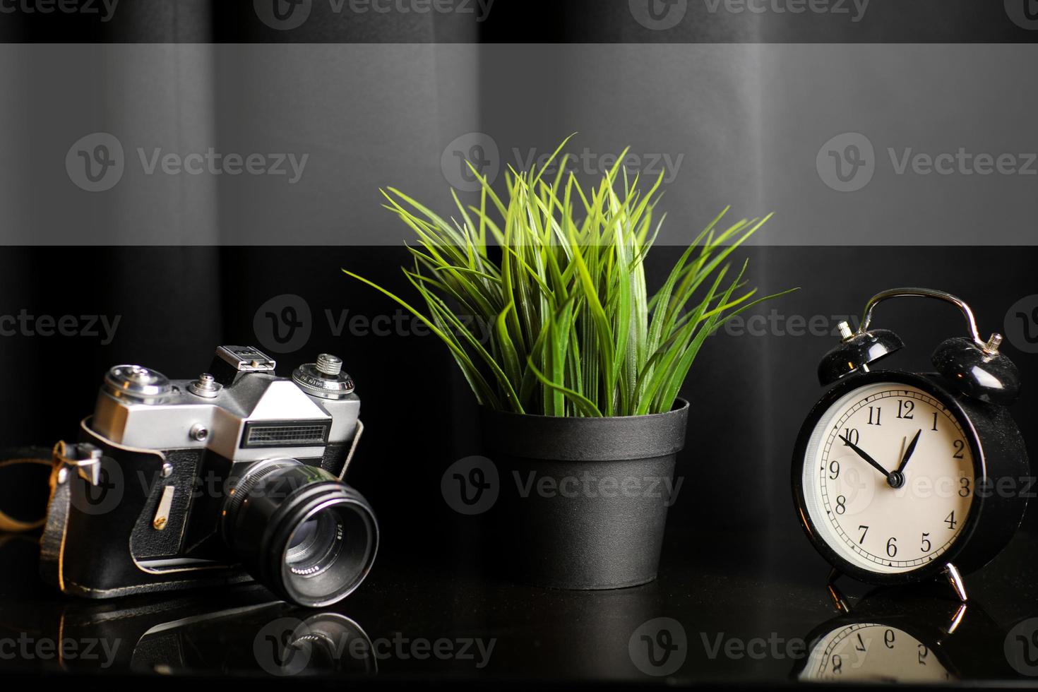 dichtbij omhoog visie van werk tafel met camera, klok en kamerplant Aan zwart tafel. hoog kwaliteit foto