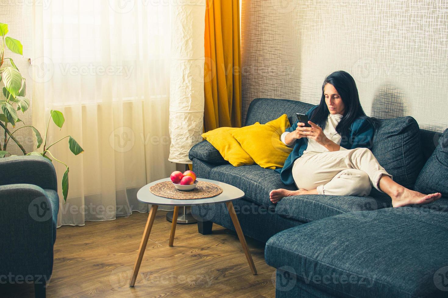 Kaukasisch modern vrouw in pak zitten Aan trainer rol Doen boodschappen doen gebruik toepassing Aan smartphone in knus modern leven kamer huis huis alleen. werk van huis genieten vrij tijd foto