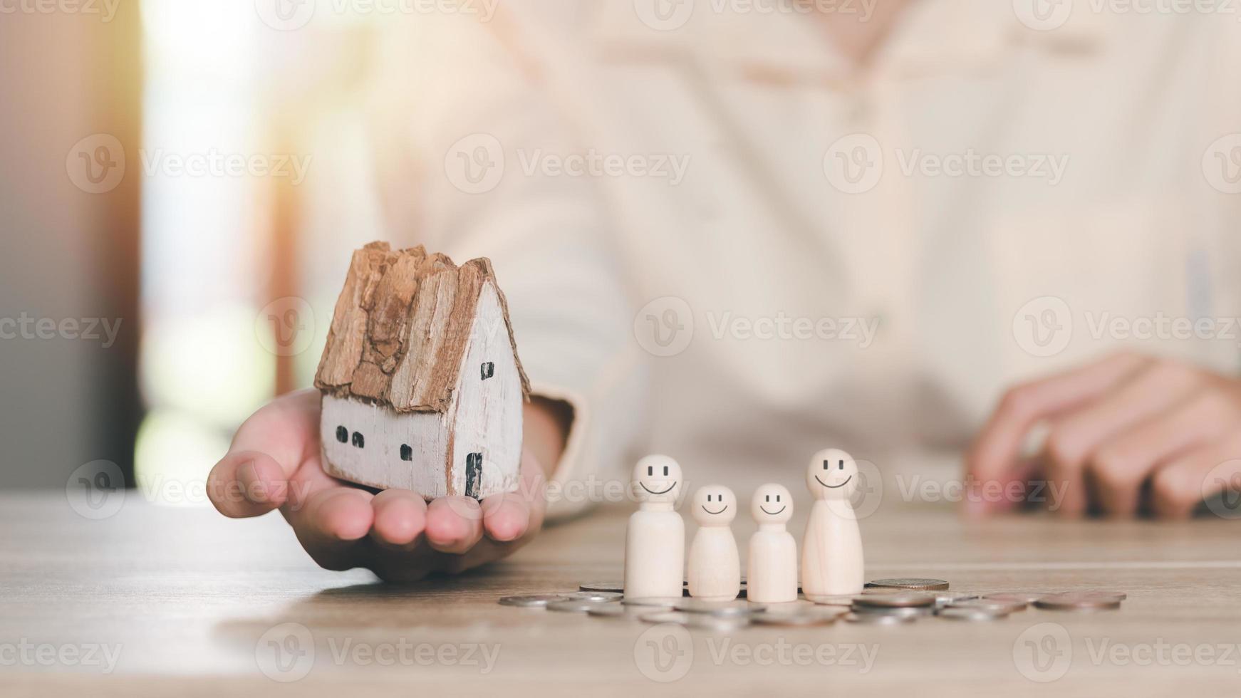 een houten huis Aan een man's hand, een houten pop en munten houdende Aan de tafel, begrip van bescherming en veiligheid bescherming, verzekering beheer planning voor beide Gezondheid en financieel veiligheid foto